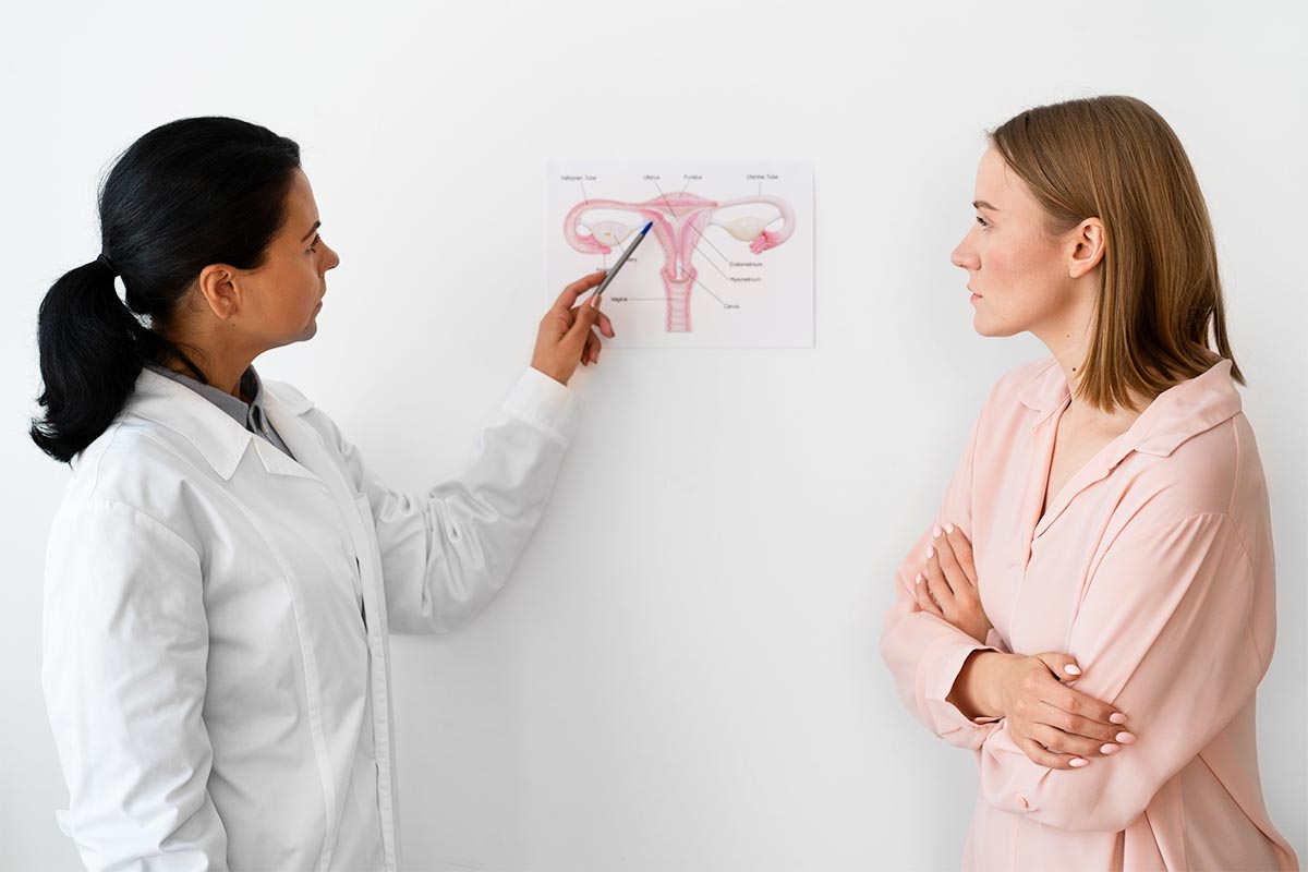Kadın doktorun duvardaki rahim anatomisi şemasını kalemle hastasına göstermesi.