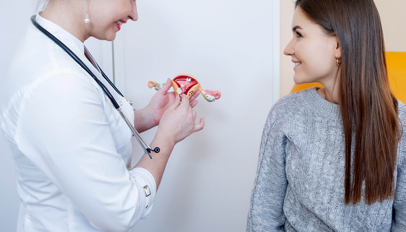 Kadın doktorun elindeki anatomik rahim modelini gülümseyerek inceleyen kadın hasta.