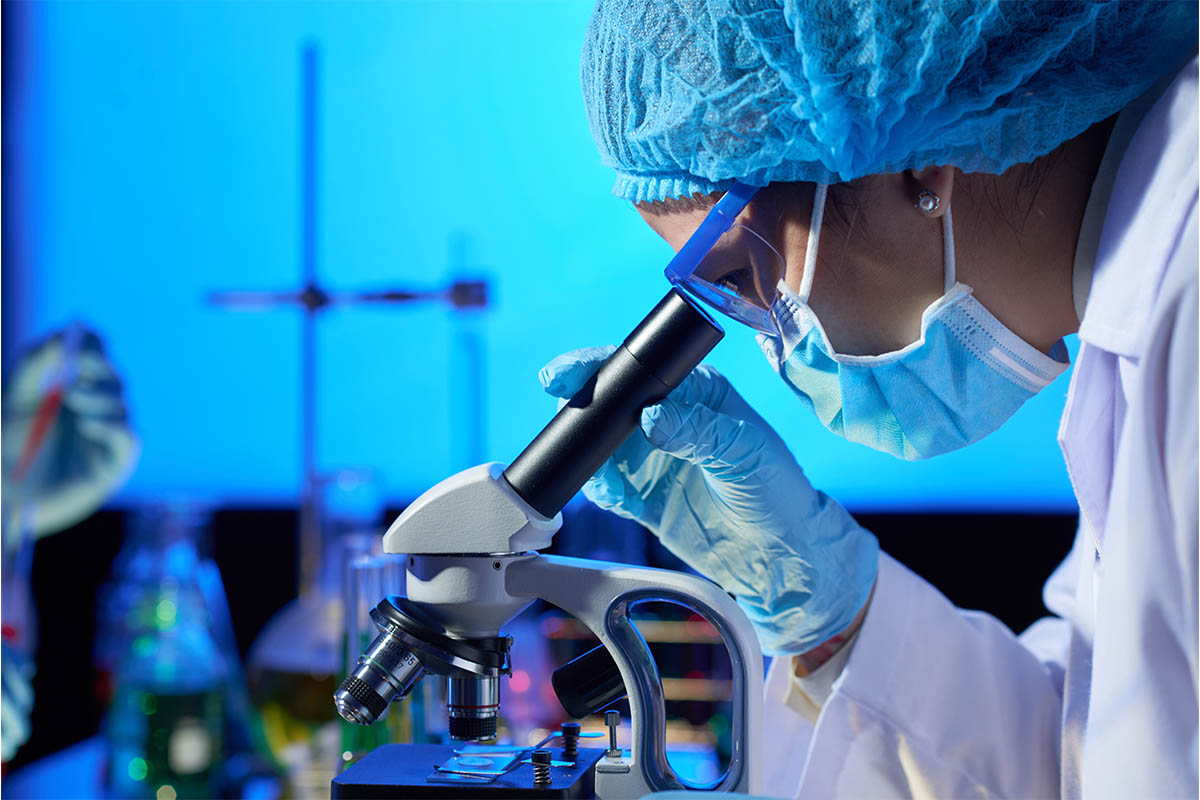 Mavi ışıklı laboratuvarda bone ve maskeli uzmanın mikroskopla çalışması.